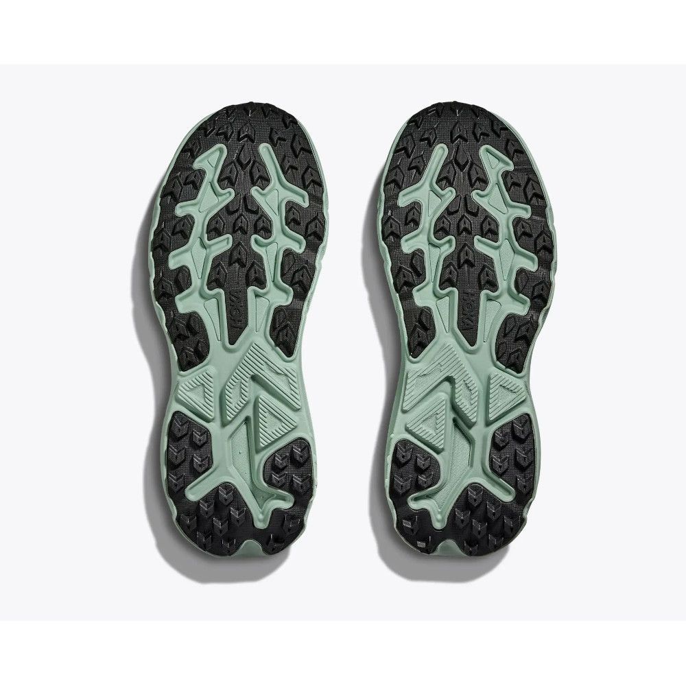 Bottom view of two trail running shoe soles in mint green and black, showing rugged tread and bold lug pattern.