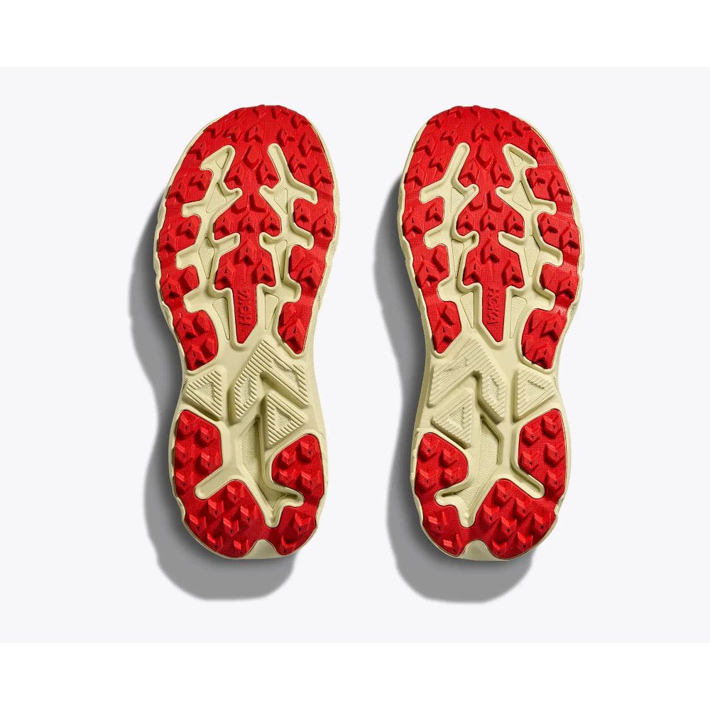 Bottom view of two red-and-cream running shoe soles with rugged tread patterns photographed from underneath