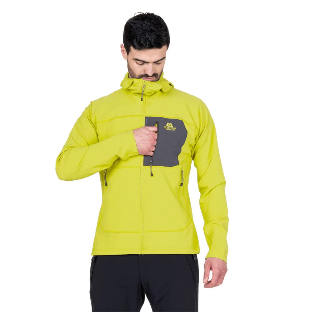 Man wearing a bright yellow outdoor jacket with a dark gray chest pocket and a logo, looking down toward the pocket.