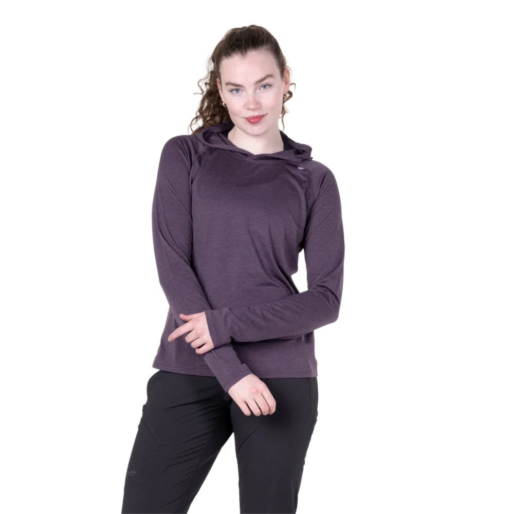 Young woman wearing a purple long-sleeve hoodie and black pants, posing with her arms crossed against a white background.