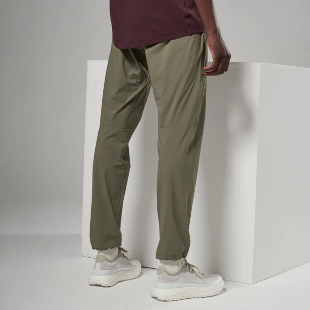 Person wearing olive-green jogger-style pants and light sneakers, standing beside a white block with one hand resting on it.