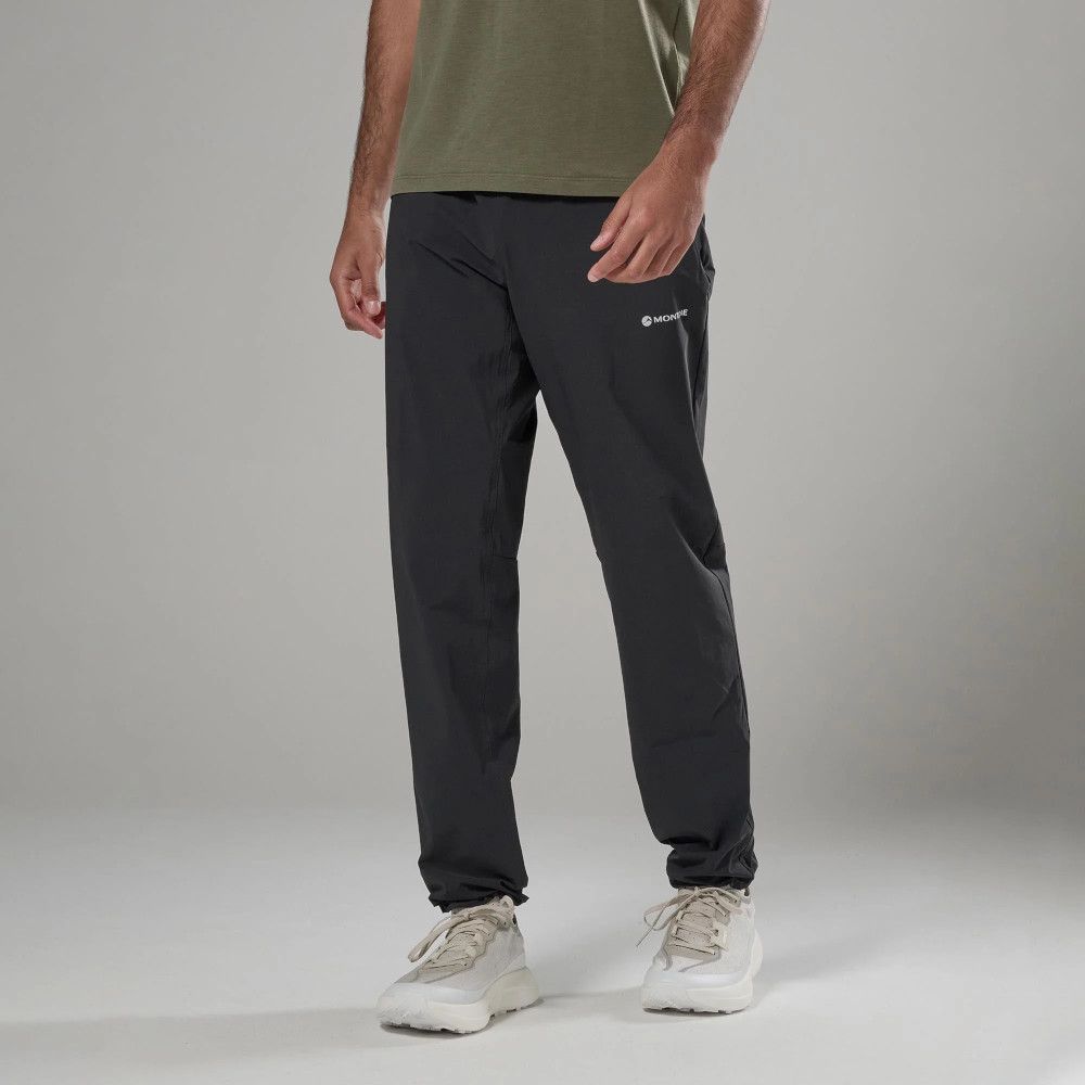 Man wearing dark gray cargo pants with a small logo on the thigh, olive shirt, and light sneakers in a studio setting.