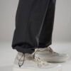 Close-up of light beige sneakers with chunky white sole, worn with black tapering pants gathered at the ankles.
