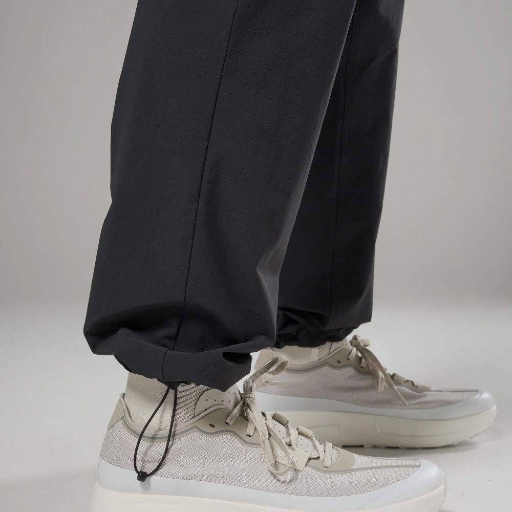 Close-up of light beige sneakers with chunky white sole, worn with black tapering pants gathered at the ankles.