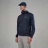 1_43c614ff-305c-487c-b528-744a22aa94cf Man modeling a navy Montane windbreaker with a small logo, wearing a blue cap and light gray pants in a studio setting.
