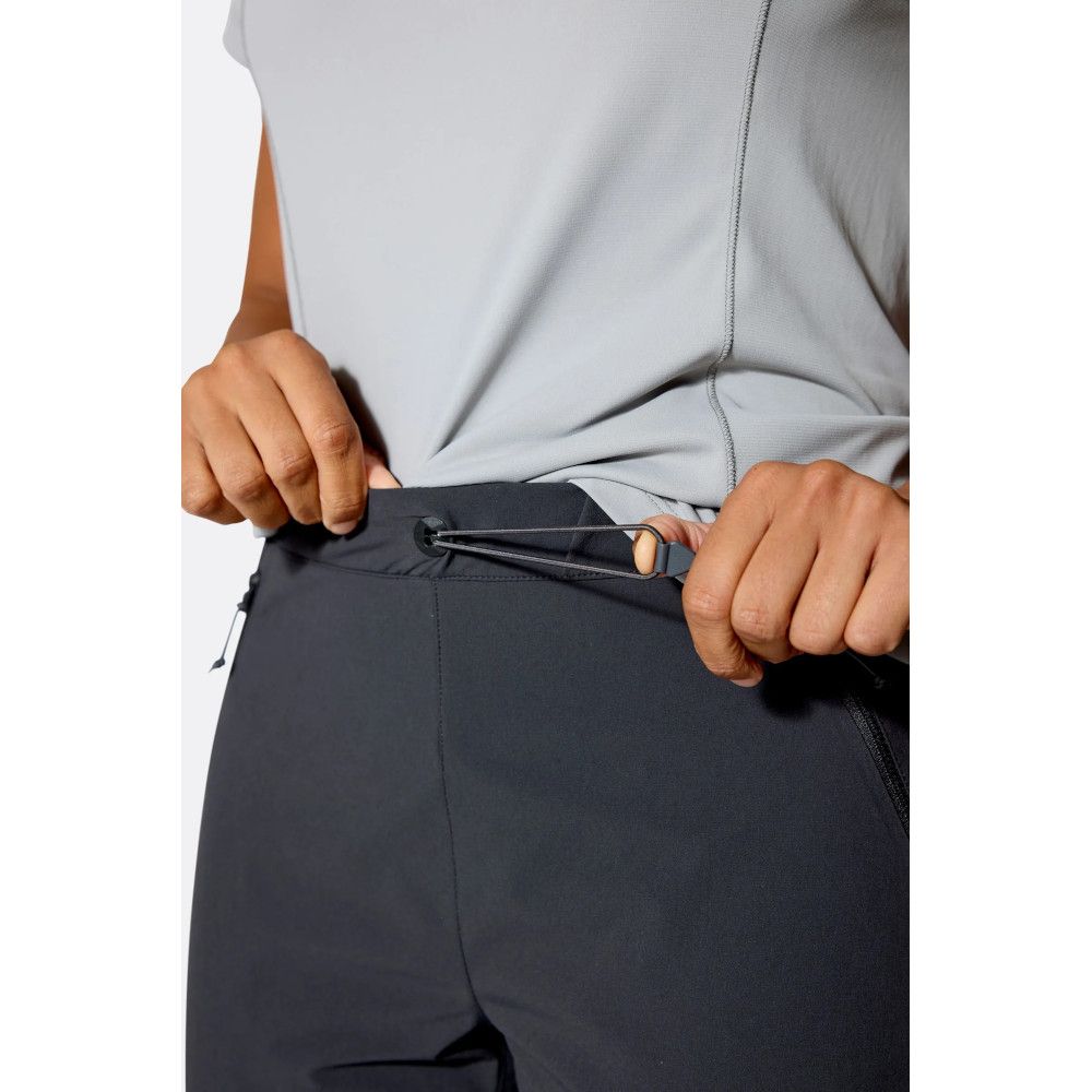 1_43c614ff-305c-487c-b528-744a22aa94cf Person cinching the adjustable waistband of dark athletic pants with a drawcord toggle.