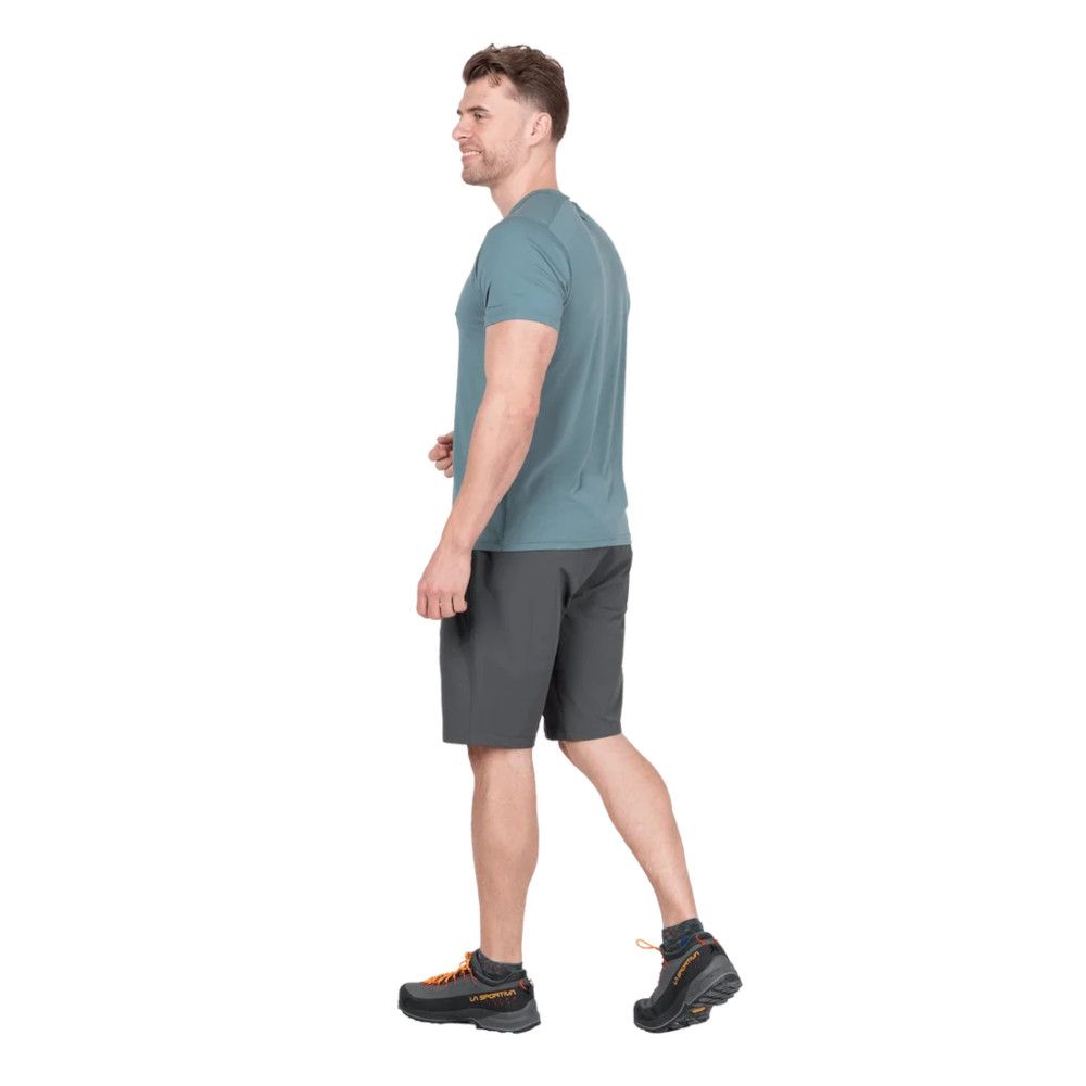 1_43c614ff-305c-487c-b528-744a22aa94cf Side view of a man in a teal T-shirt and dark shorts walking, wearing black trail shoes with orange laces
