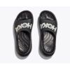 1_43c614ff-305c-487c-b528-744a22aa94cf Pair of black Hoka slide sandals photographed from above, showing a large white logo on each strap on a light background.