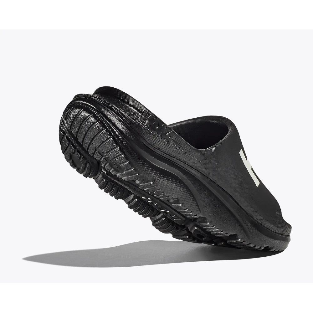 1_43c614ff-305c-487c-b528-744a22aa94cf Black slip-on athletic shoe shown at an angle to highlight the rugged tread outsole and side silhouette