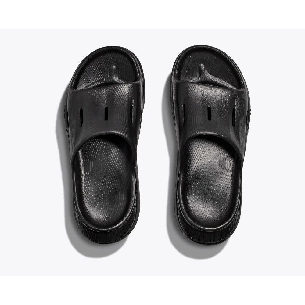 Pair of black slide sandals viewed from above on a light background, showing open-toe design and textured footbeds.