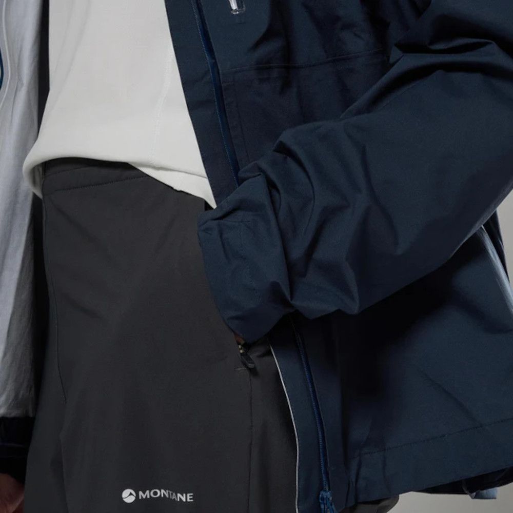 1_43c614ff-305c-487c-b528-744a22aa94cf Close-up of a dark navy Montane waterproof jacket over a white top and black hiking pants; zipper visible on the jacket.
