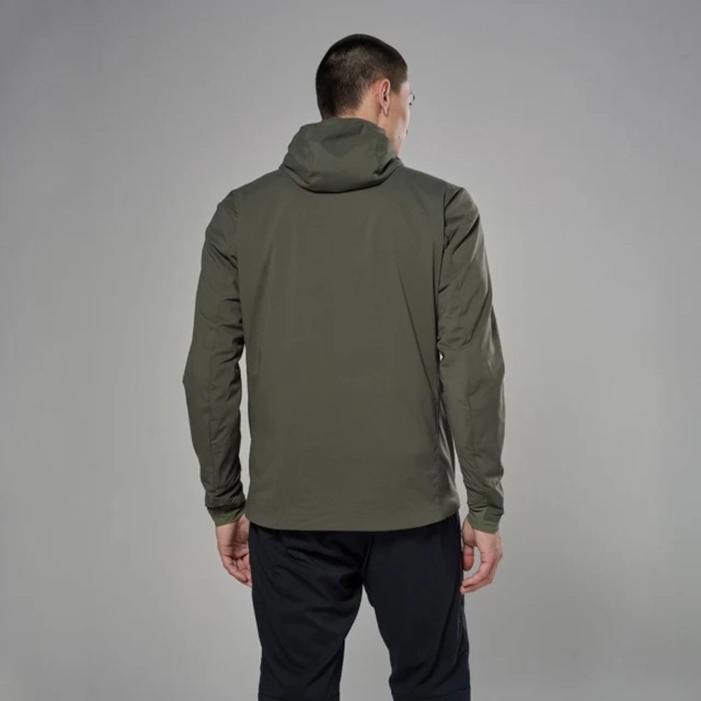 Person standing with back to camera in an olive-green hooded jacket and dark pants on a gray backdrop.