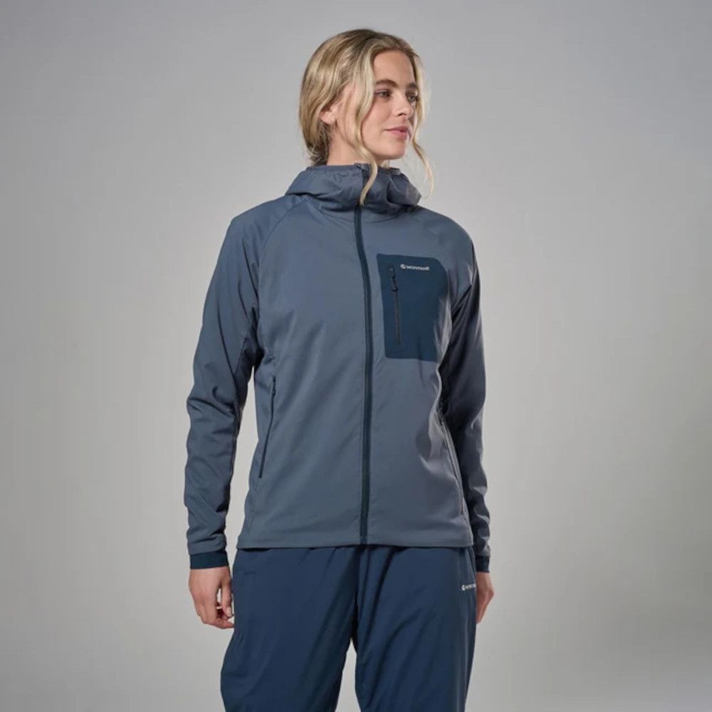 1_43c614ff-305c-487c-b528-744a22aa94cf Woman wearing a two-tone blue softshell jacket with a chest zip pocket and side pockets, paired with matching blue pants, posing in a studio setting.