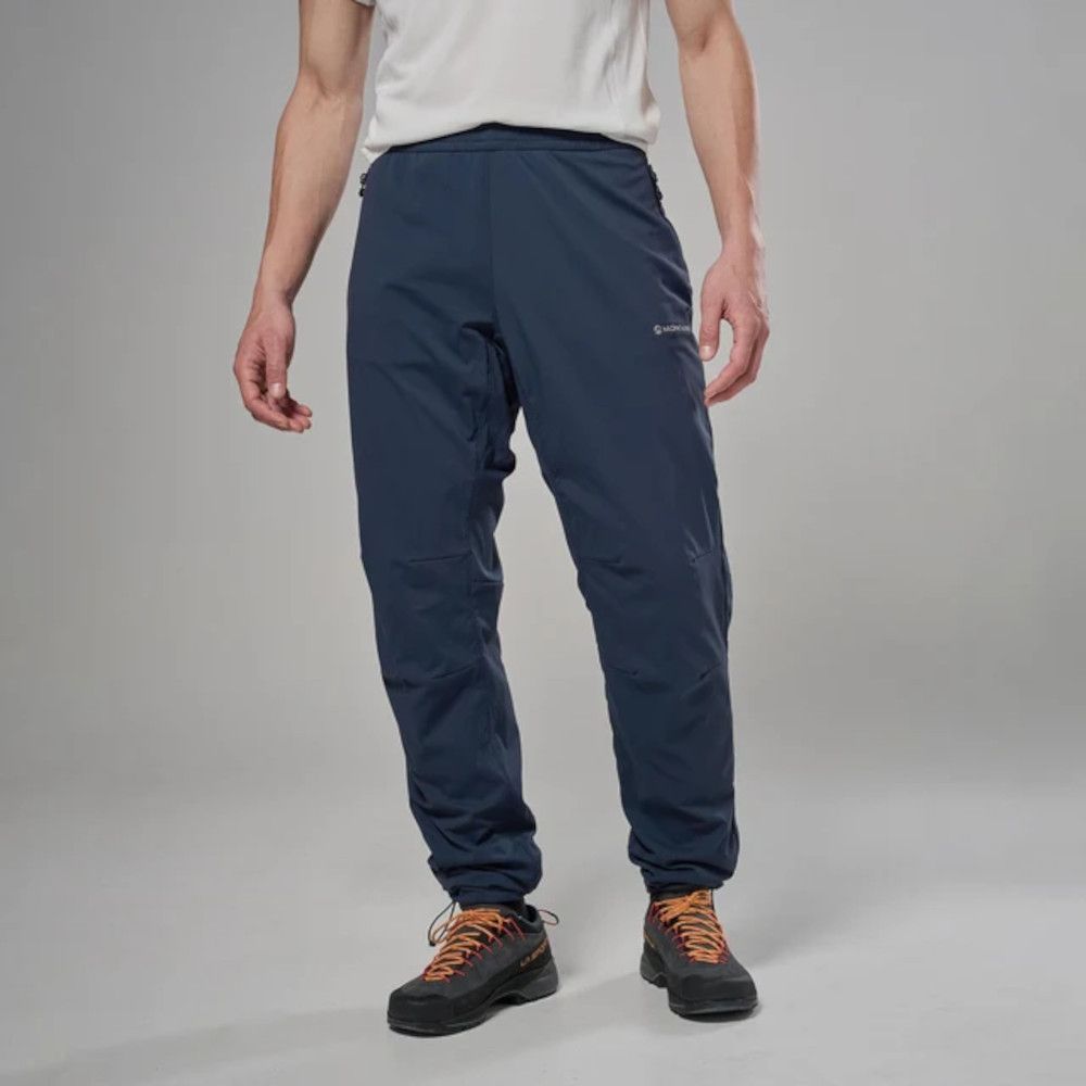 Person wearing navy outdoor pants with cinched ankles and orange-lace hiking boots, standing against a gray studio backdrop.