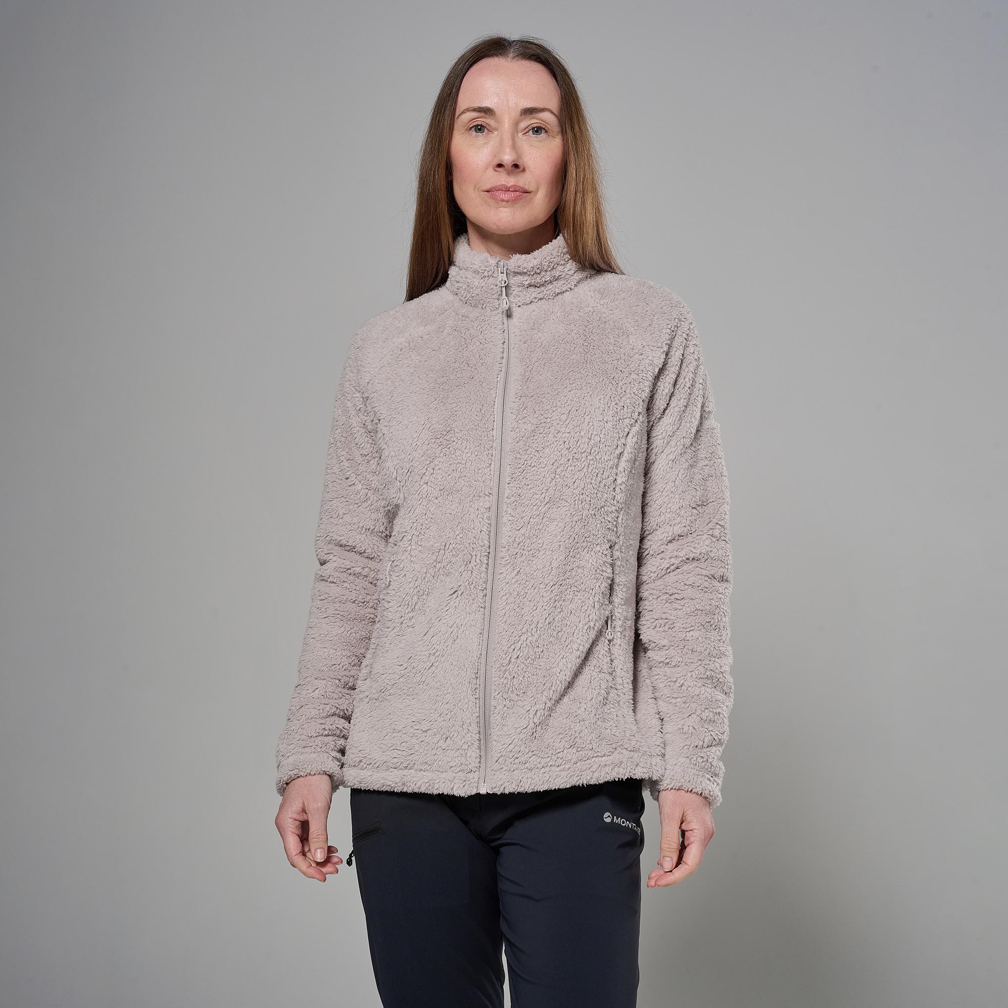 Woman standing in a light beige fleece zip-up jacket against a plain gray backdrop, full body view.