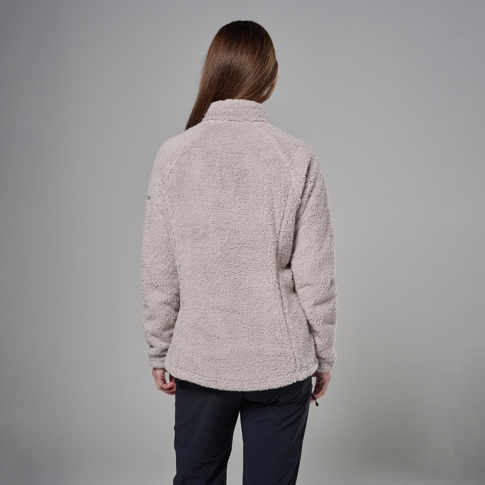 Back view of a person wearing a plush beige fleece jacket and dark pants, standing against a gray background.
