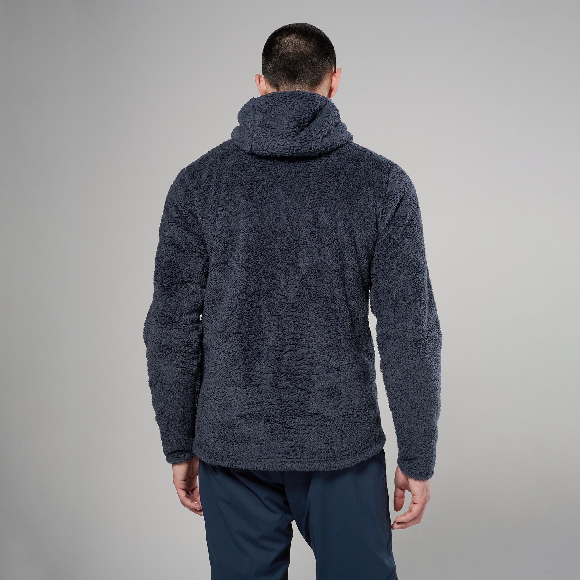 MCXTH_DAS_A_2_square_d2b219e4-86e9-47a9-a3ac-f18aff6f1526 Back view of a person wearing a dark, textured fleece jacket with a hood, standing against a gray background.