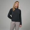 Woman modeling a black long-sleeve top and light gray pants in a studio against a neutral gray backdrop, with wavy blonde hair.