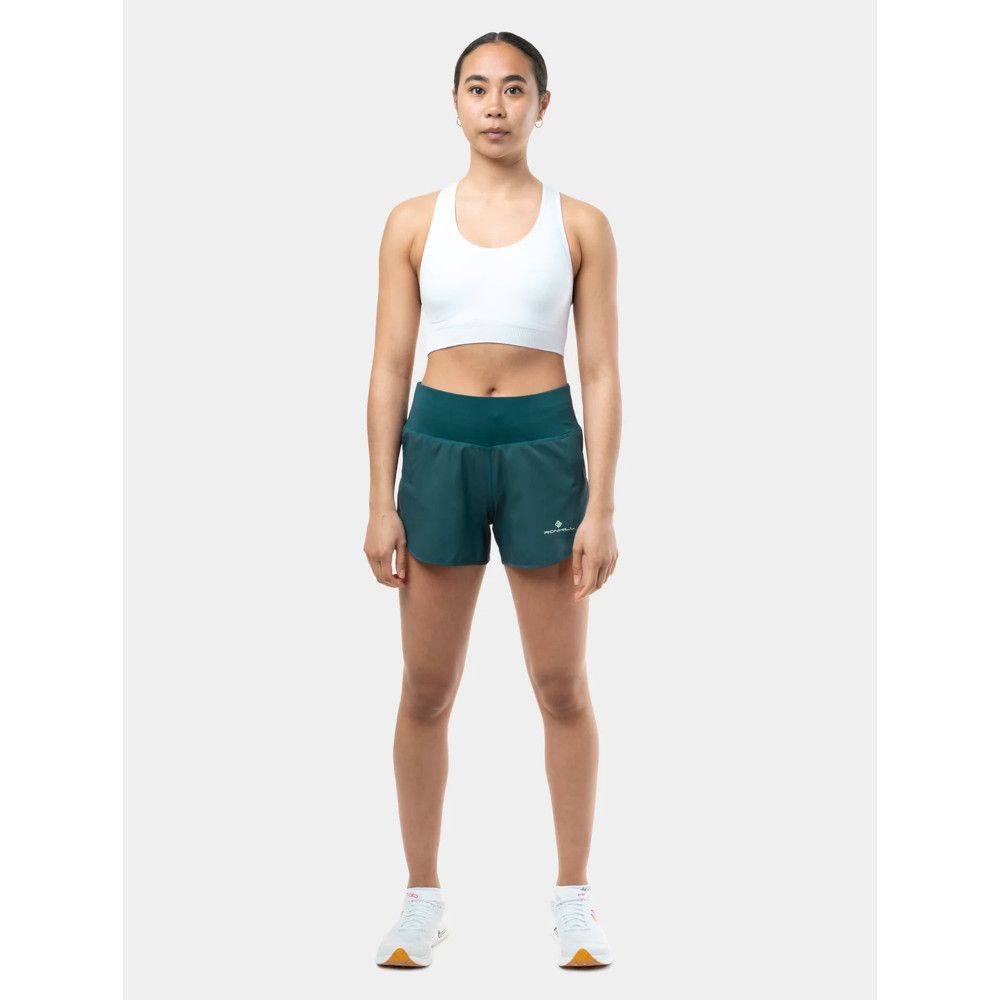 MKLPR_ECL_P_1_square_b214d799-76b2-4a64-a0ae-a2325d30818b_640x Woman wearing a white sports bra and teal running shorts, standing facing the camera with arms relaxed at her sides and white sneakers.