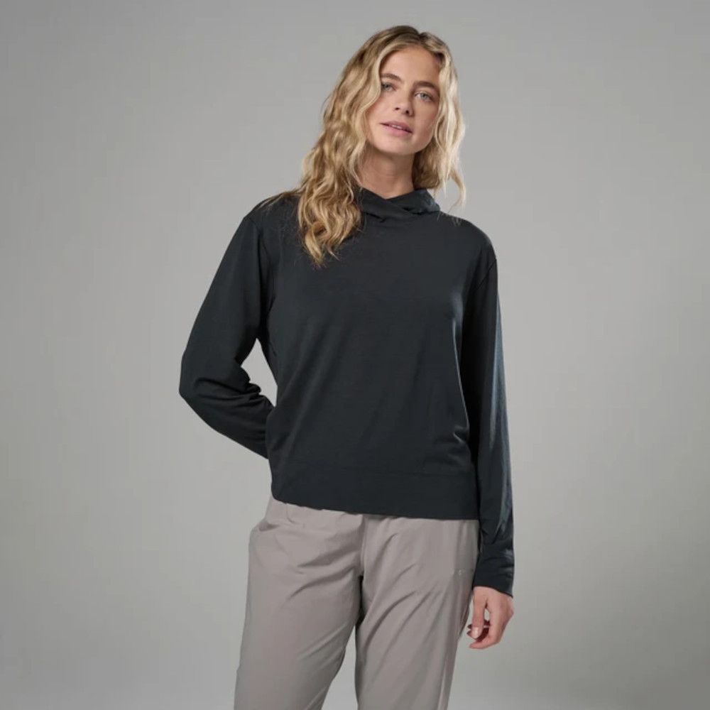Woman modeling a black long-sleeve top and light gray pants in a studio against a neutral gray backdrop, with wavy blonde hair.